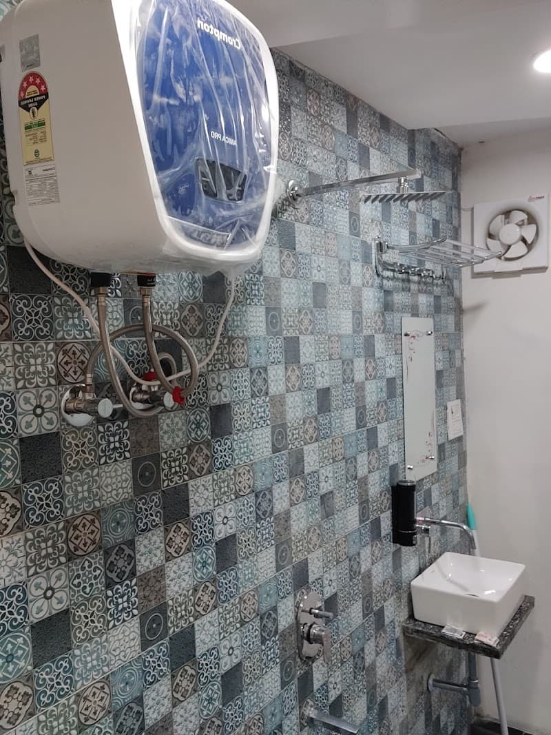 A cozy bathroom at Jhansi Castle Inn features patterned blue tiles, a wall-mounted water heater, and modern fixtures, creating a functional and inviting space for travelers seeking comfort in Jhansi, Uttar Pradesh.