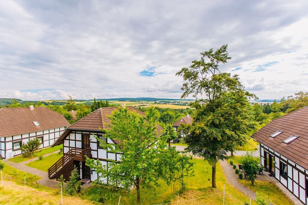 A serene countryside retreat features charming half-timbered houses nestled among lush greenery under a partly cloudy sky, ideal for travelers seeking a peaceful rural getaway.