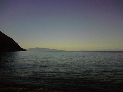A serene lakeside scene at dusk, featuring calm waters, distant hills under a twilight sky, ideal for tranquil evening walks or photography.