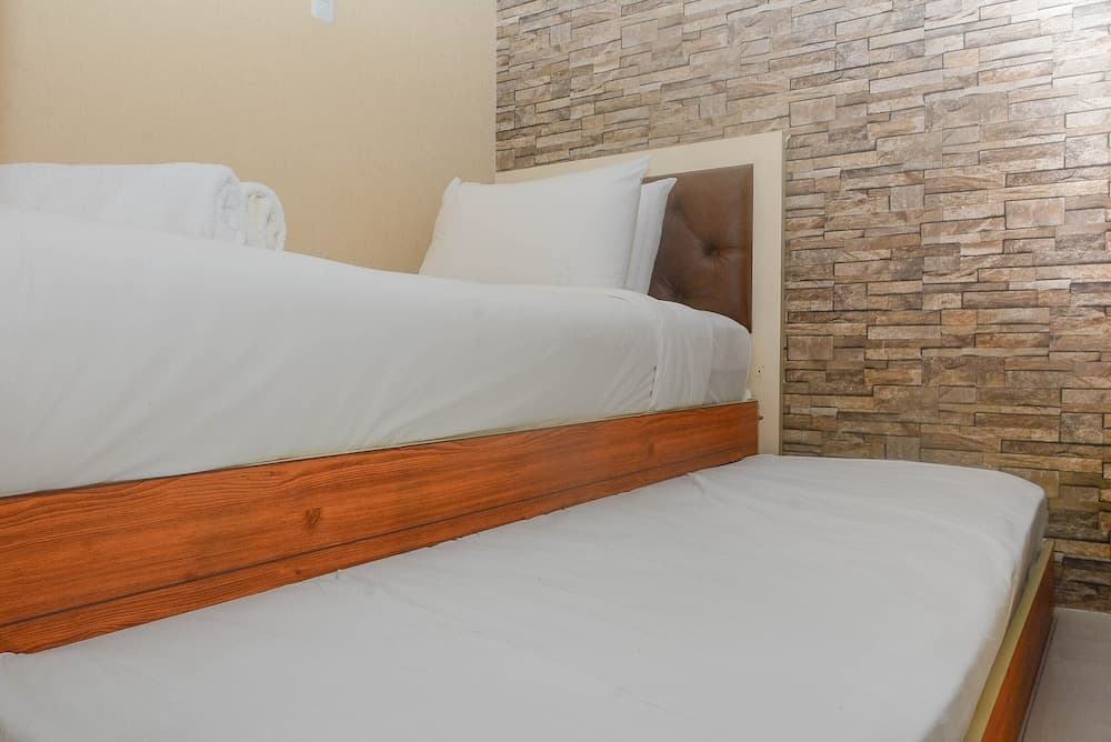 A cozy hotel room features two neatly made beds with white linens against a rustic brick wall, ideal for travelers seeking comfort and simplicity.