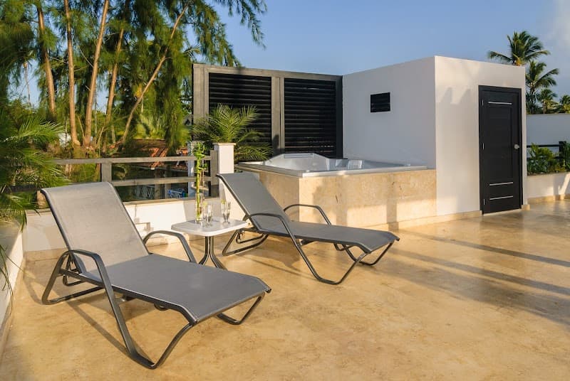 A serene rooftop terrace in Las Terrenas, Dominican Republic, features modern lounge chairs, a hot tub, lush tropical greenery, and a tranquil ambiance perfect for a relaxing vacation getaway.