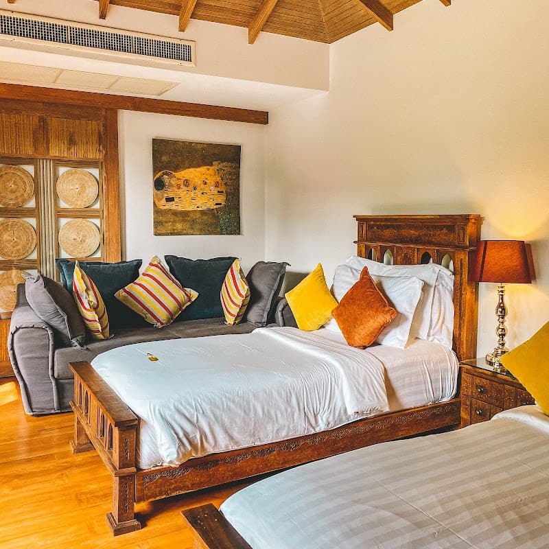 A cozy, tropical-themed bedroom at Tango Luxe on Koh Samui features a wooden bed adorned with colorful pillows, a plush sofa, and warm lighting, ideal for travelers seeking a serene and luxurious retreat.