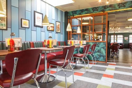A vibrant retro diner with colorful striped flooring, red leather booths, and eclectic decor offers a nostalgic dining experience ideal for travelers seeking a unique local eatery.