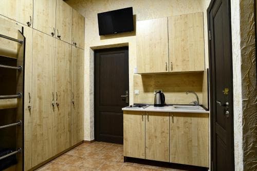 A cozy kitchenette with wooden cabinets, a sink, and a mounted TV creates a warm and functional space ideal for travelers seeking comfort in a compact apartment setting.