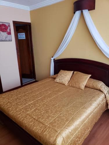 A cozy hotel room features a neatly made bed adorned with golden bedding under a draped canopy, set against warm yellow walls, ideal for travelers seeking comfort and relaxation.