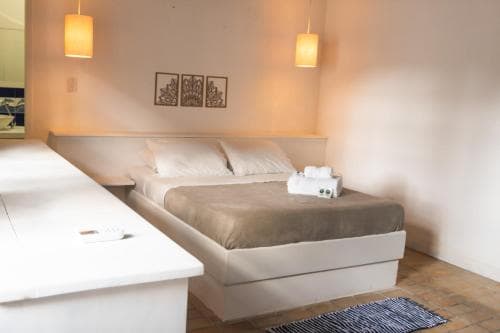A cozy hotel room features a neatly made bed with white linens, warm wall-mounted lamps, and a minimalist design, ideal for travelers seeking comfort and simplicity.