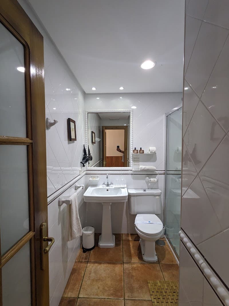 A cozy, well-lit bathroom in a Spanish accommodation features white tiled walls, a sink, toilet, shower area, and neatly arranged towels, ideal for travelers seeking comfort and cleanliness.