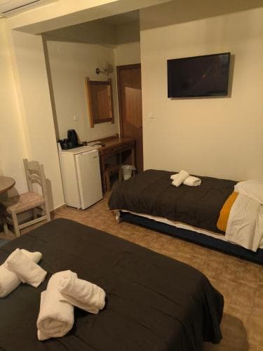 A cozy hotel room with two neatly made beds, a small kitchenette, and a mounted TV creates a welcoming atmosphere ideal for budget travelers seeking comfort and convenience.