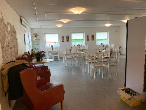 A cozy café space features white tables and chairs set against bright windows, with a relaxed atmosphere enhanced by red armchairs and floral decorations, ideal for travelers seeking a quiet spot to unwind or work remotely.