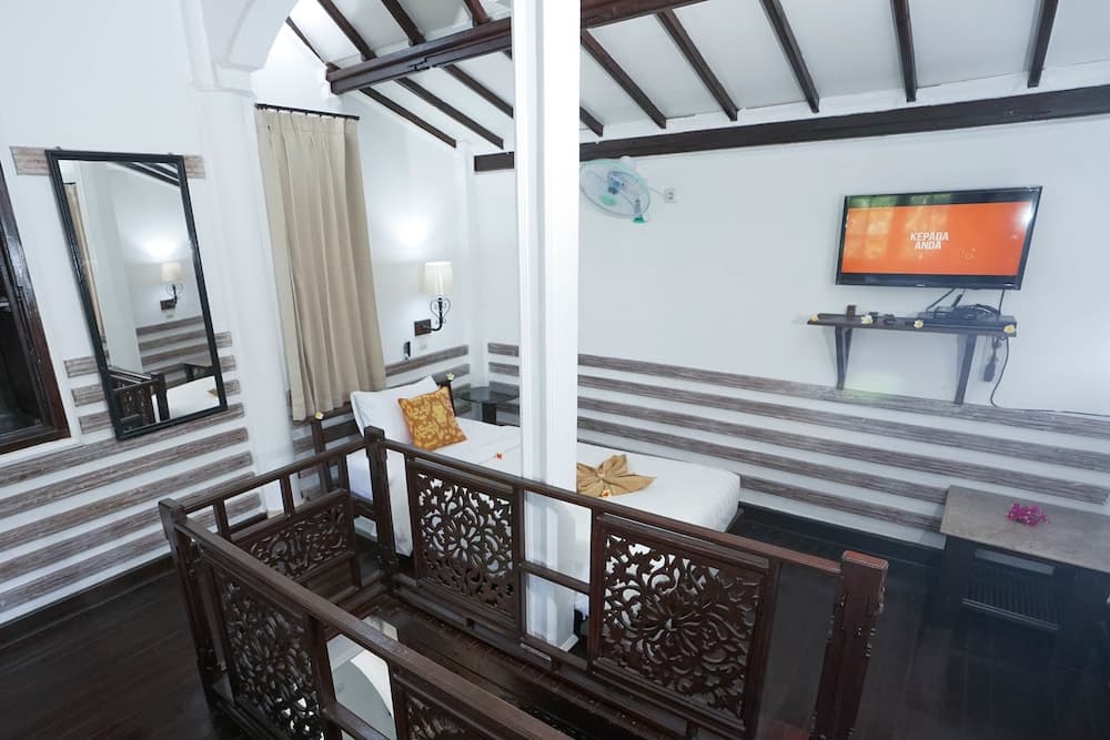 A cozy loft-style bedroom with wooden beams, ornate railings, and a mounted TV creates an inviting atmosphere ideal for travelers seeking a charming and comfortable stay.