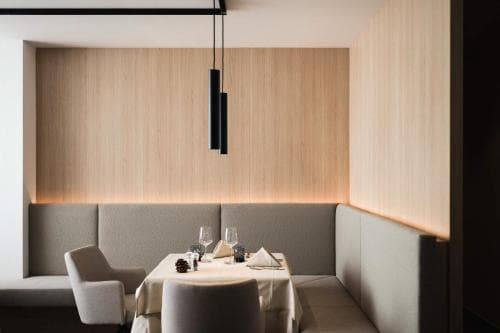 A cozy modern dining area features sleek wooden walls, soft lighting, and minimalist decor, creating an intimate atmosphere ideal for upscale restaurant experiences.