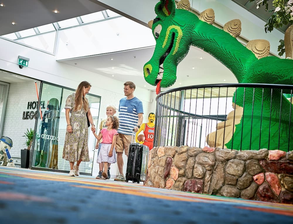 A cheerful family explores a vibrant indoor theme park area featuring a giant LEGO dragon sculpture, ideal for family-friendly travel experiences.