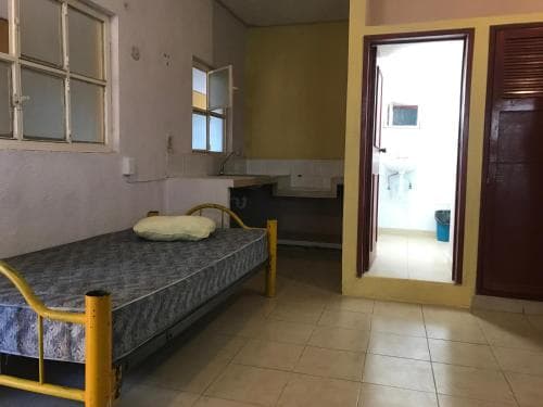 A simple hostel room with a single bed, tiled floors, and an open doorway leading to a bright bathroom, ideal for budget travelers seeking basic accommodations.