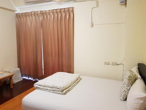 A cozy bedroom with a neatly made bed, patterned curtains, and soft lighting creates a serene atmosphere, ideal for travelers seeking a comfortable and quiet accommodation.