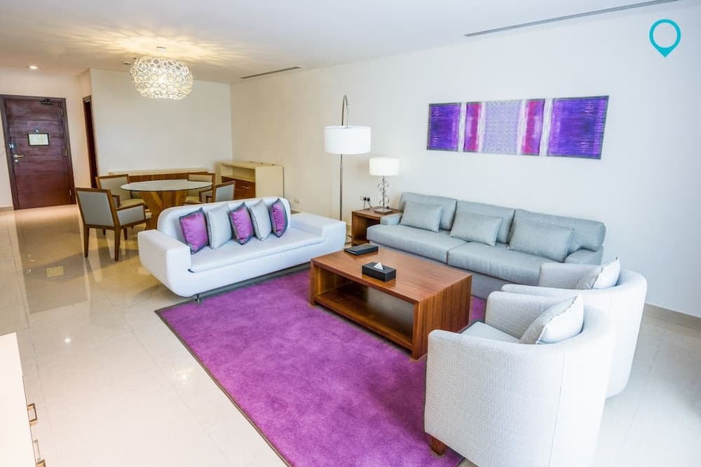 A modern living room with sleek furniture, a vibrant purple rug, and contemporary art creates a cozy yet stylish atmosphere ideal for travelers seeking a comfortable stay in a chic apartment.