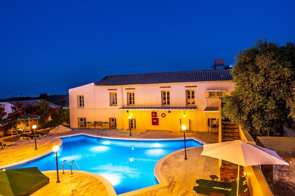 A serene evening at a Mediterranean villa features a glowing pool, cozy lounge areas, and warm ambient lighting, ideal for travelers seeking relaxation and luxury.