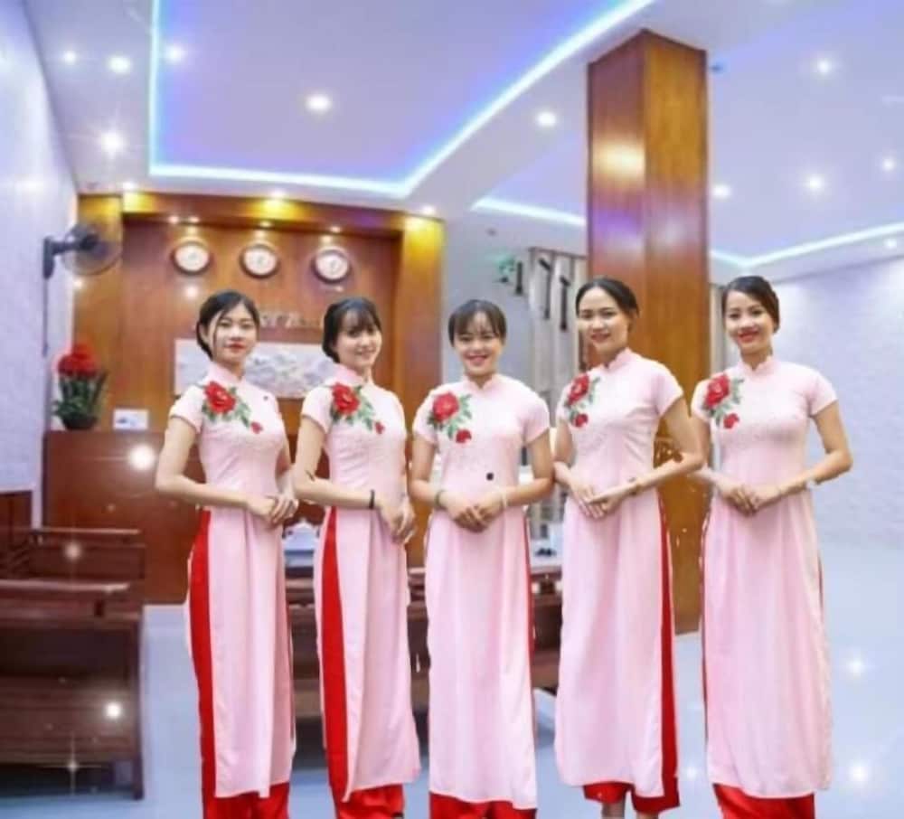 Five women in elegant pink and red traditional dresses stand warmly in a modern hotel lobby adorned with decorative lighting and wooden accents, ideal for travelers seeking cultural hospitality experiences.