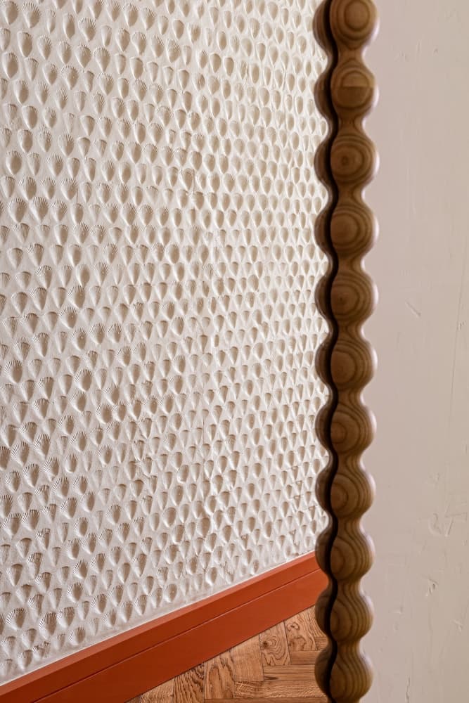A close-up of an intricately textured wall adorned with shell-like patterns and a scalloped wooden frame creates a cozy, artistic indoor ambiance perfect for interior design enthusiasts exploring unique architectural details.