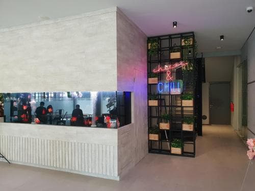 A modern restaurant entrance featuring a neon "Cheese & Chili" sign, sleek concrete decor, and a view into the dining area through glass panels, ideal for travelers seeking trendy dining spots.
