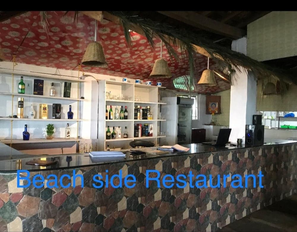 A cozy beachside restaurant with a vibrant mosaic bar, stocked shelves of drinks, woven pendant lights, and a relaxed tropical vibe, perfect for travelers seeking a laid-back dining experience by the sea.