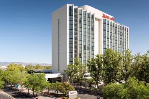 A towering Marriott hotel stands amidst lush greenery under a clear blue sky, offering travelers a modern urban retreat with easy access to nearby amenities.