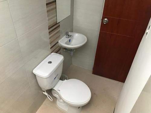A compact bathroom with beige tiles, a white toilet, sink, and mirror exudes cleanliness and simplicity, ideal for travelers seeking basic amenities in budget accommodations.