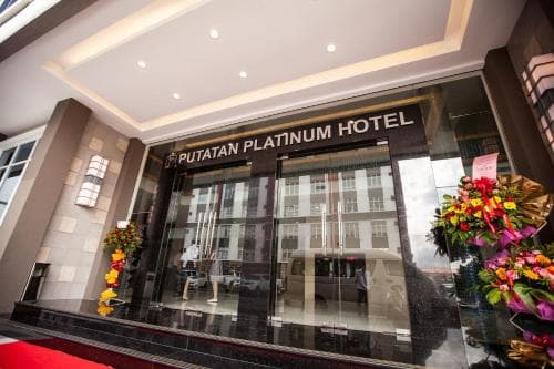 A modern hotel entrance featuring the "Putatan Platinum Hotel" sign, vibrant floral arrangements, and sleek glass doors, exudes a welcoming and upscale atmosphere ideal for travelers seeking comfort and style.