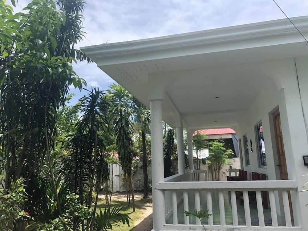 A serene tropical villa with a white veranda and lush greenery offers a peaceful retreat for travelers seeking relaxation in a natural setting.
