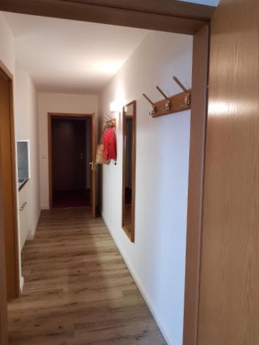 A cozy apartment hallway with wooden flooring, white walls, and a coat rack adorned with jackets, ideal for travelers seeking comfortable accommodations.