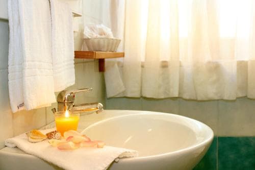 A serene hotel bathroom features a white sink adorned with a lit candle, rose petals, and neatly folded towels, creating a tranquil ambiance ideal for relaxation and wellness retreats.