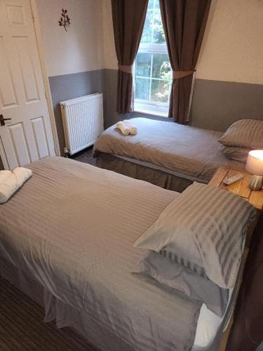 A cozy twin-bedded room with neatly arranged beds, soft lighting, and a window view of greenery, ideal for travelers seeking a comfortable and peaceful accommodation experience.