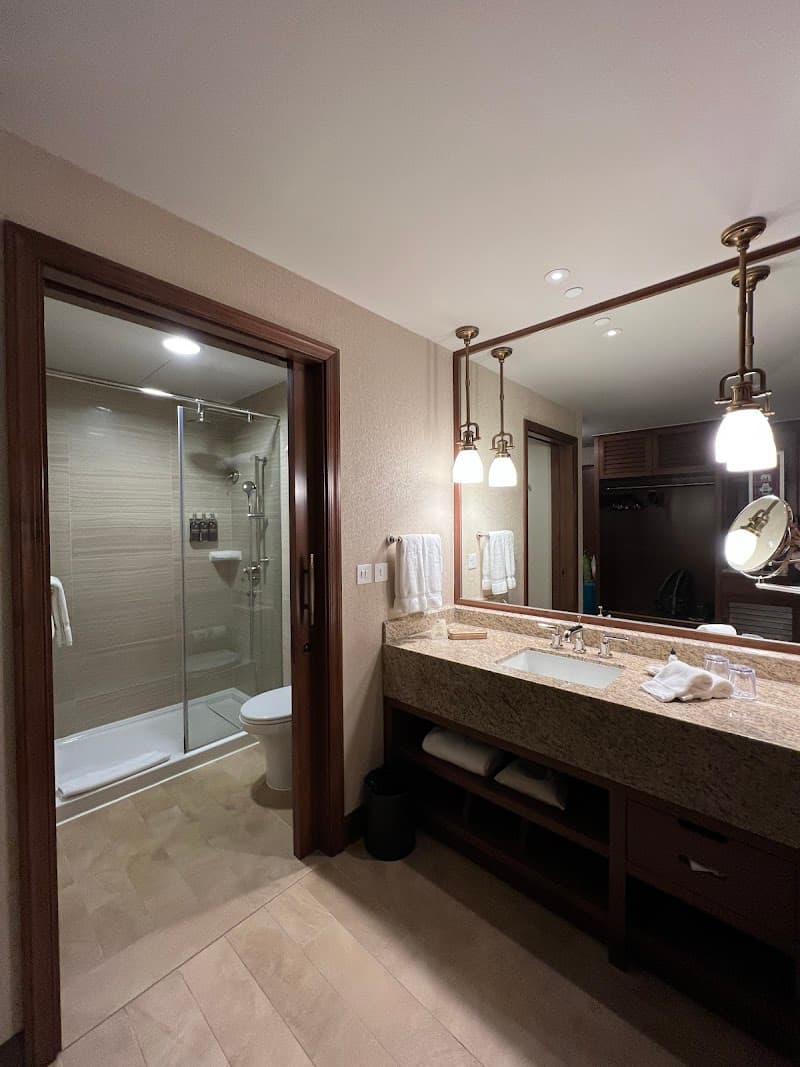 A cozy hotel bathroom at Disney Explorers Lodge in Hong Kong features a modern shower, granite countertop, and warm lighting, ideal for travelers seeking comfort and luxury.