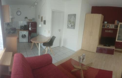 A cozy apartment interior featuring a compact kitchen, dining area, and living space with warm tones and functional furniture, ideal for travelers seeking a comfortable short-term stay in an urban setting.