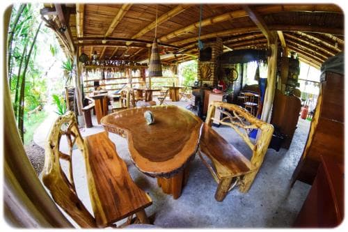 A cozy, rustic café with natural wooden furniture and a thatched roof invites travelers to relax amidst lush greenery, perfect for a serene dining experience.