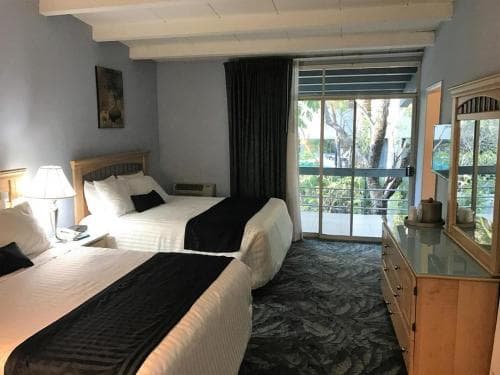 A cozy hotel room with two neatly made beds, a glass door leading to a lush outdoor view, and warm lighting creates an inviting atmosphere ideal for travelers seeking relaxation.