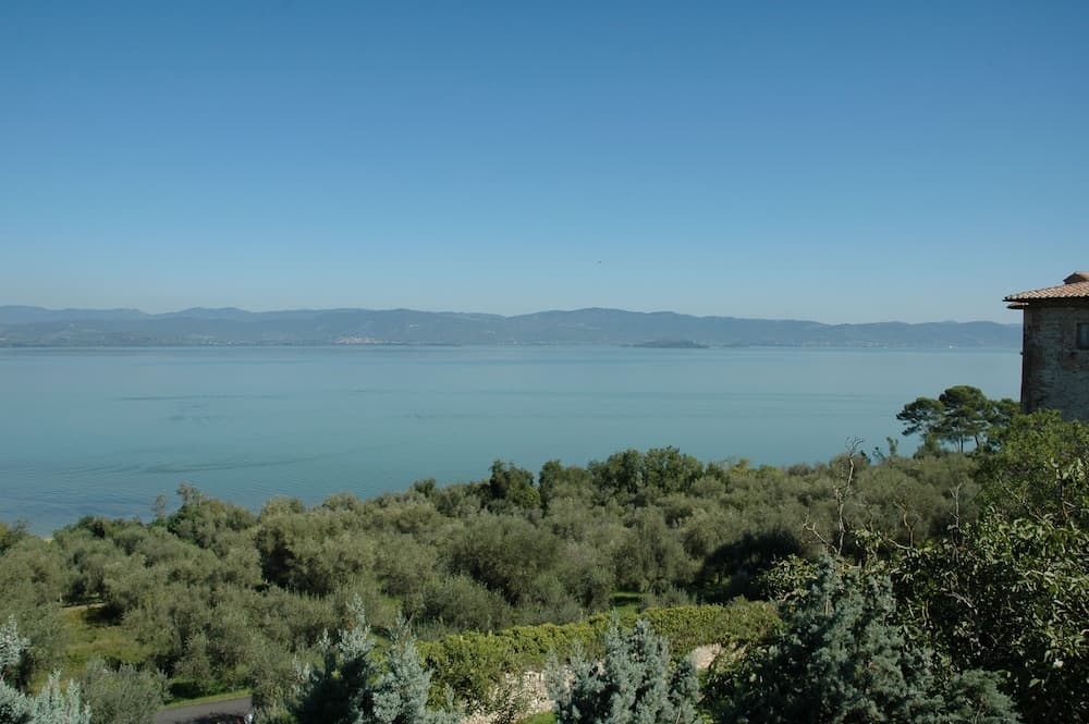 A serene lakeside vista with lush greenery, distant mountains under a clear blue sky, and a rustic building corner, ideal for tranquil retreats and nature photography.