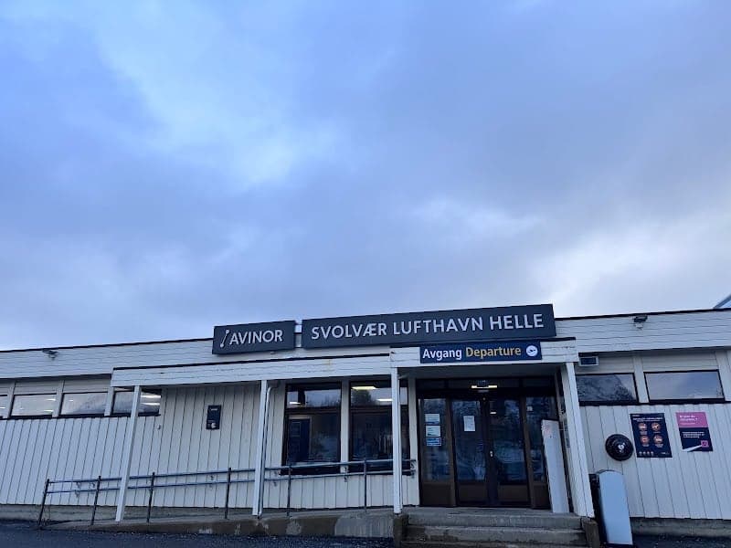 A serene view of Svolvær Lufthavn Helle in Norway under a cloudy sky, featuring a modest airport terminal with clear signage, ideal for travelers seeking a gateway to the Arctic region.