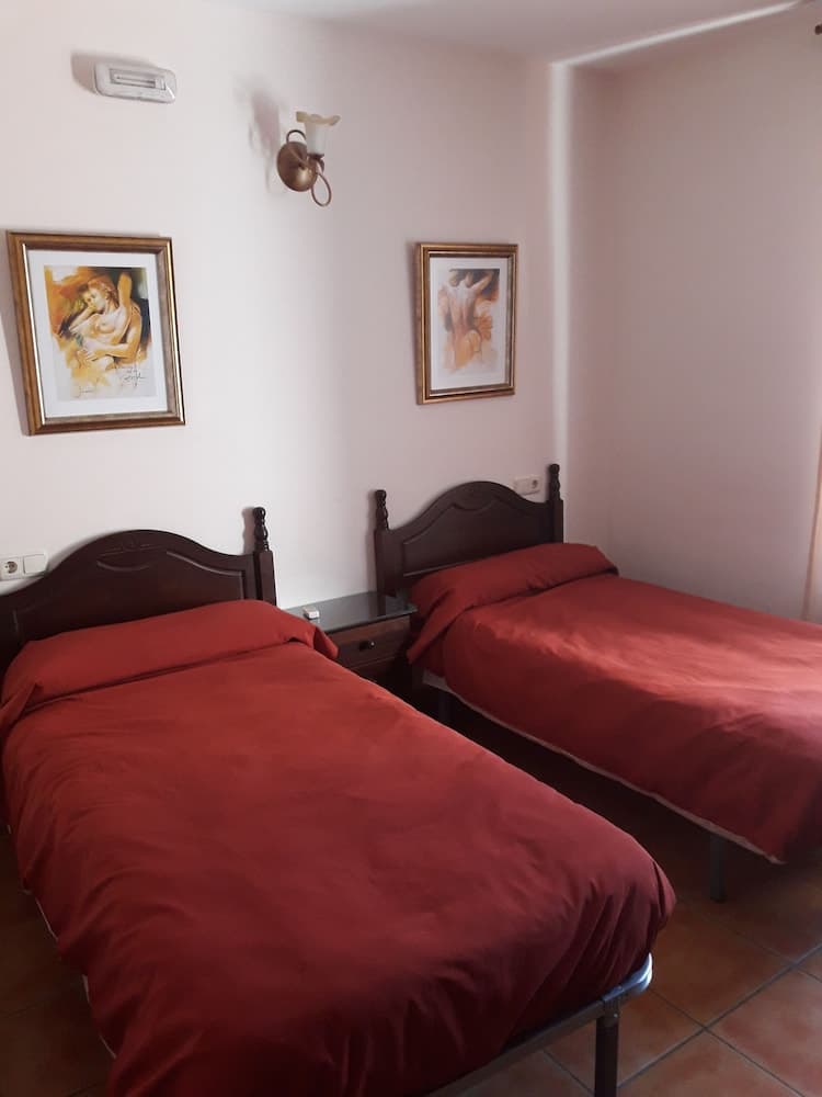 A cozy hotel room features two single beds with red linens, framed artwork on the walls, and a warm ambiance, ideal for travelers seeking comfortable budget accommodations.