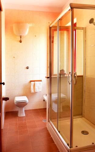 A cozy bathroom with terracotta tiles, a glass-enclosed shower, and warm lighting creates an inviting atmosphere, perfect for travelers seeking comfort in their accommodations.