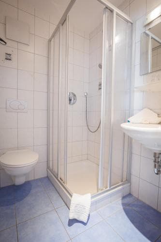 A clean, compact bathroom with white tiled walls, a glass-enclosed shower, blue floor tiles, and neatly arranged towels creates a functional and inviting space ideal for travelers seeking comfort in accommodations.