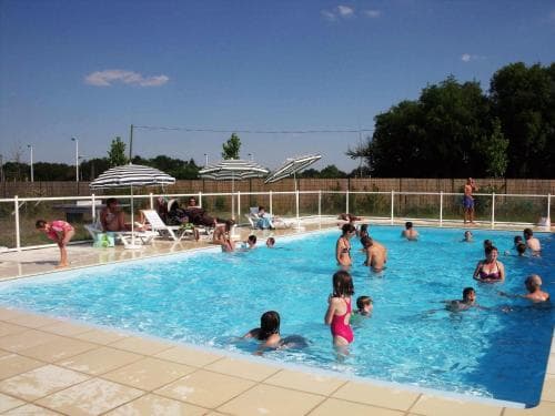A lively outdoor swimming pool scene under a clear blue sky, featuring people enjoying the water, lounge chairs, umbrellas, and a fenced perimeter, ideal for family vacations or leisurely getaways.