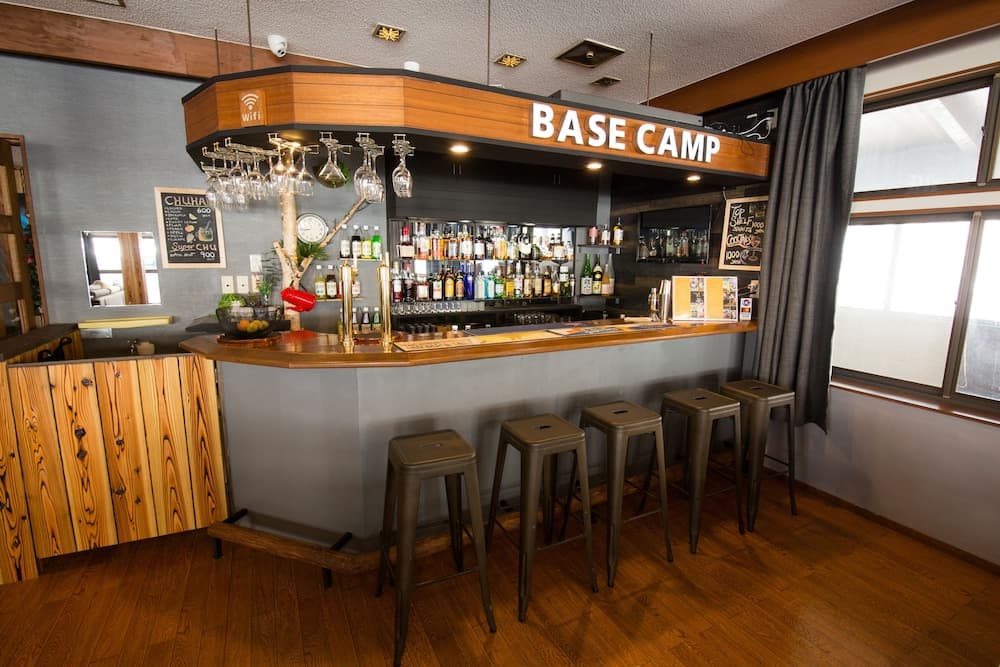 A cozy bar named "BASE CAMP" features wooden accents, metal stools, and a well-stocked liquor shelf, creating an inviting atmosphere perfect for travelers seeking relaxation and refreshments.