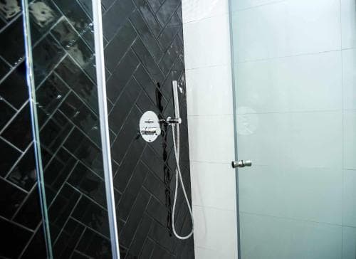 A modern bathroom shower with sleek black tiles, glass doors, and a handheld showerhead creates a clean and luxurious ambiance, ideal for travelers seeking comfort in upscale accommodations.