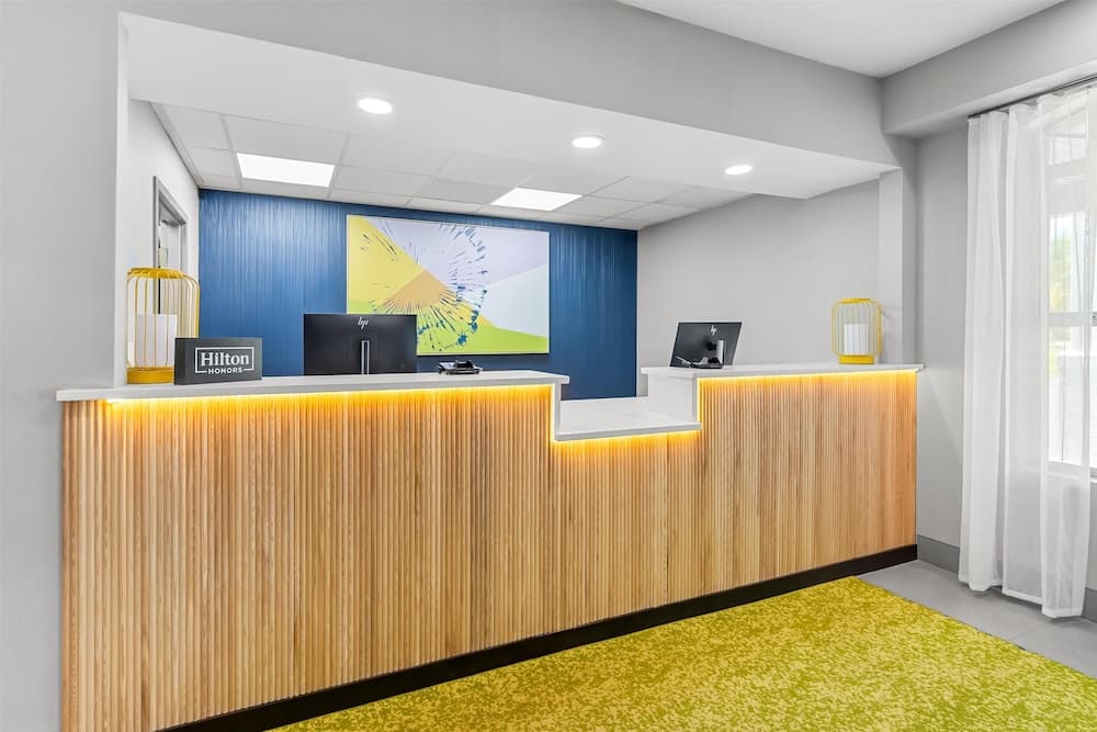 A modern hotel reception area features a sleek wooden desk with warm lighting, a vibrant yellow carpet, and contemporary decor, creating an inviting atmosphere ideal for travelers seeking comfort and style.