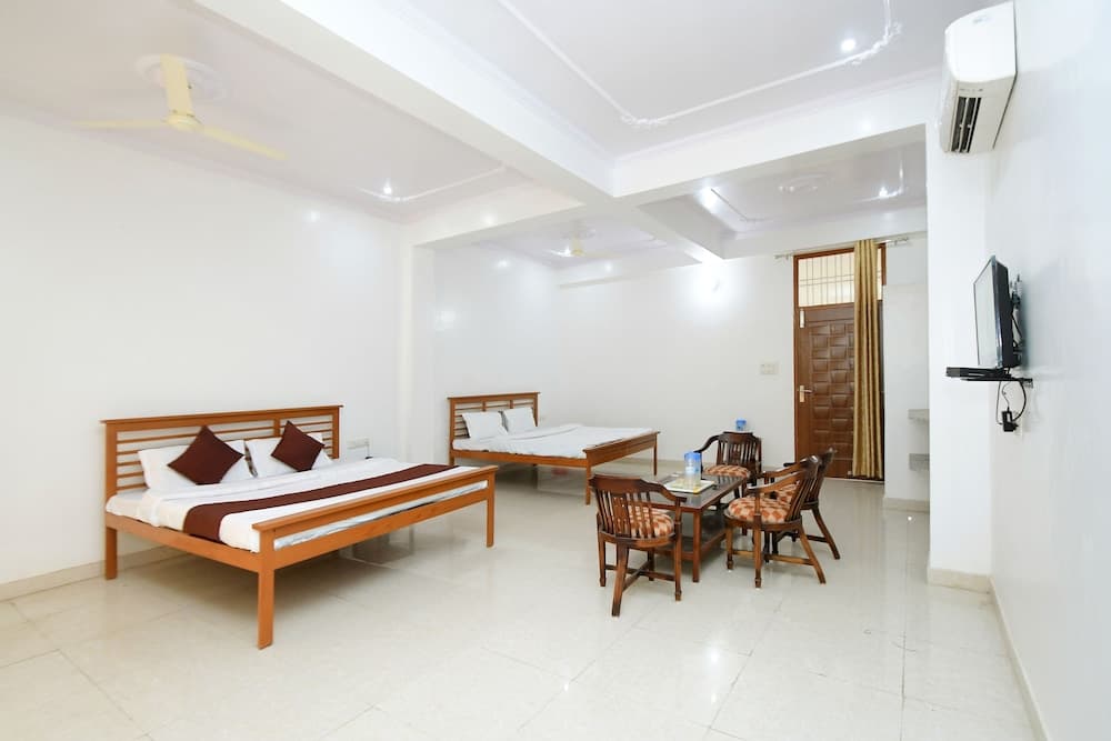 A cozy hotel room features two wooden beds, a dining area with chairs, a mounted TV, and a ceiling fan, ideal for travelers seeking comfort and functionality in a clean, well-lit space.