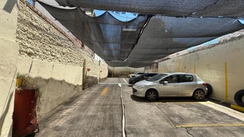 A shaded urban alleyway lined with parked cars under a canopy of netting offers a quiet respite, ideal for travelers seeking a peaceful route through the city.