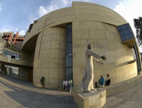 A serene urban plaza features a striking modern statue in front of a curved concrete building, inviting travelers to explore its cultural significance and architectural design.