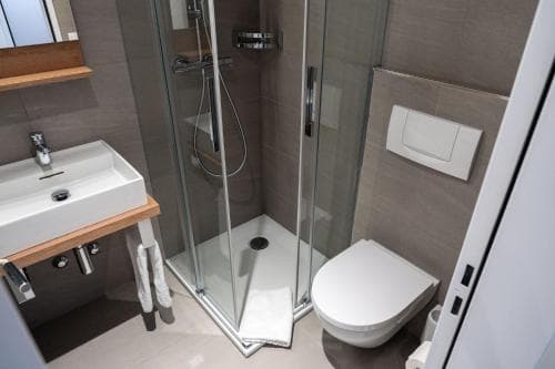 A modern bathroom with sleek fixtures, a glass-enclosed shower, and minimalist design evokes a clean and serene atmosphere, ideal for travelers seeking comfort in compact spaces.