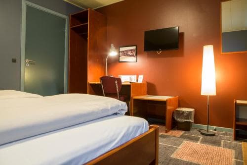 A cozy hotel room with warm orange walls, a neatly made bed, modern furnishings, and ambient lighting creates an inviting atmosphere ideal for travelers seeking comfort and relaxation.