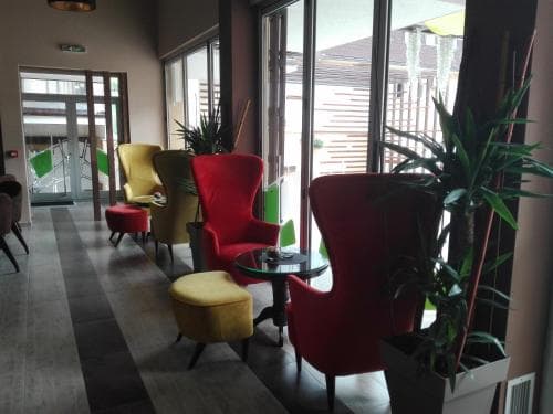 A cozy hotel lobby features vibrant red and yellow armchairs paired with matching ottomans, lush green plants, and large windows offering a serene view of an outdoor deck, ideal for travelers seeking relaxation and comfort during their stay.